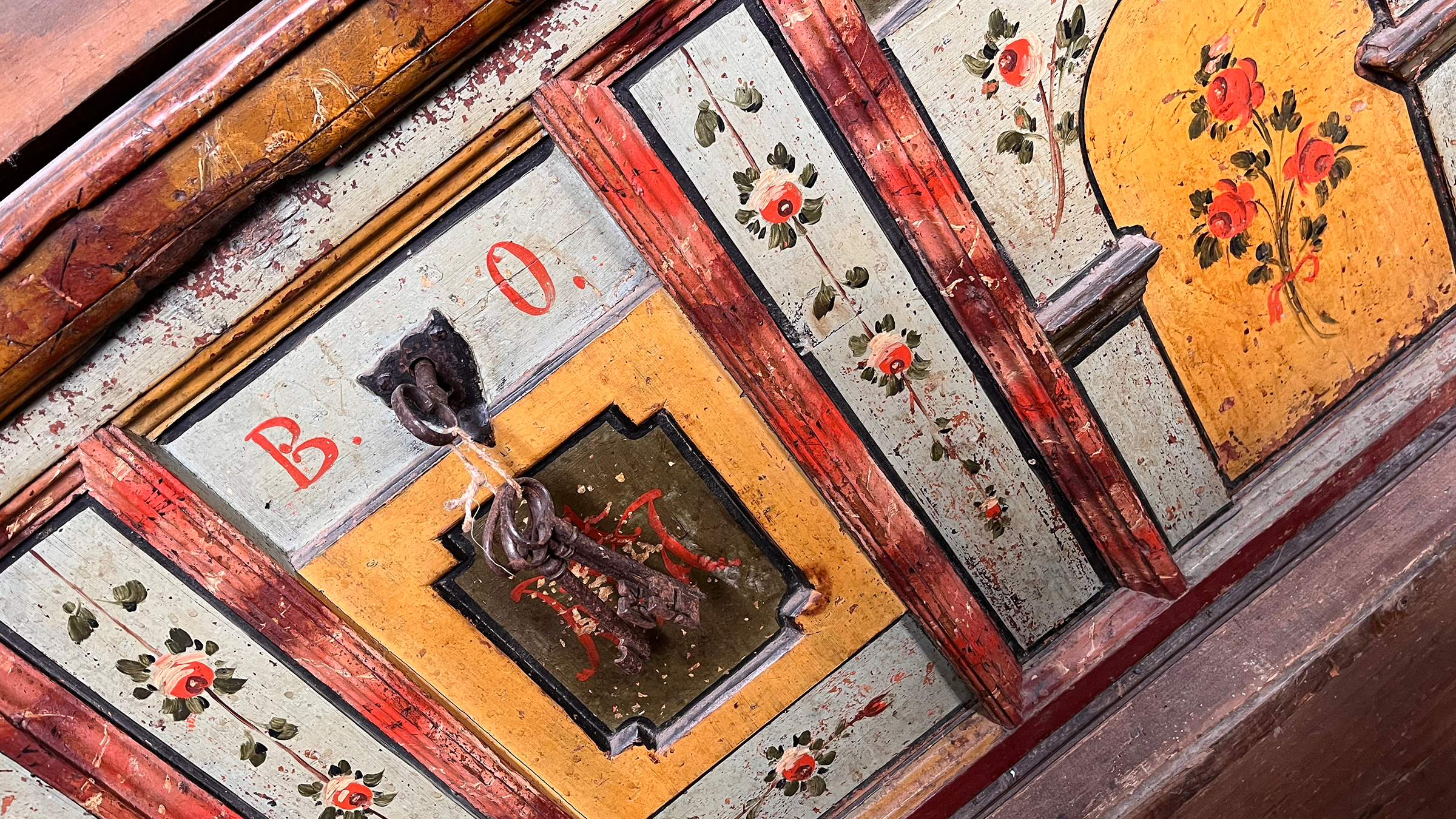 Historische Holztruhe, bemalt mit Blumen und Zierelementen in grün, gelb und rot.