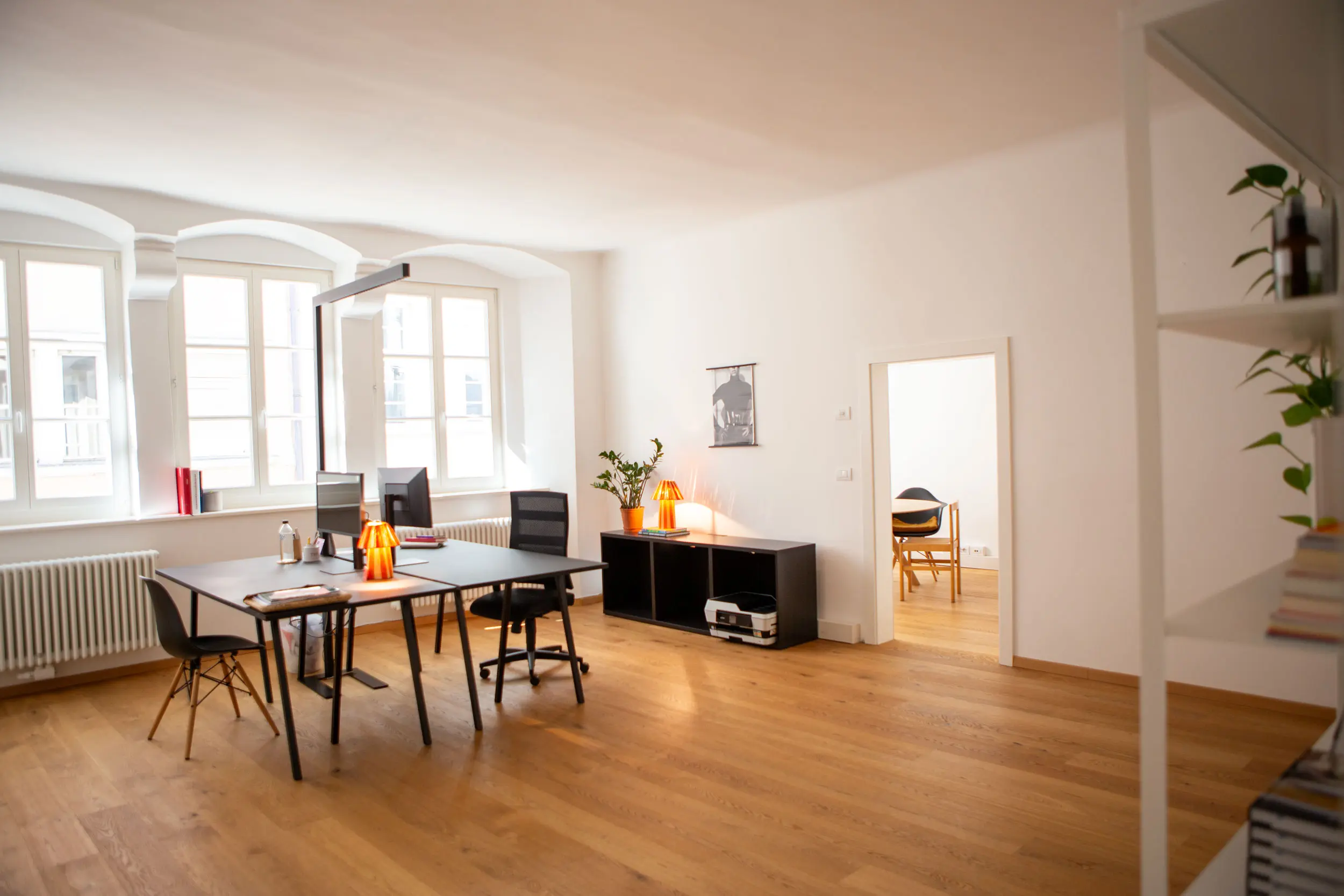 Heller Büroraum der Kreativagentur i-kiu design mit großen Fenstern und zwei dunklen Schreibtischen mit Monitoren und Bürostühlen.