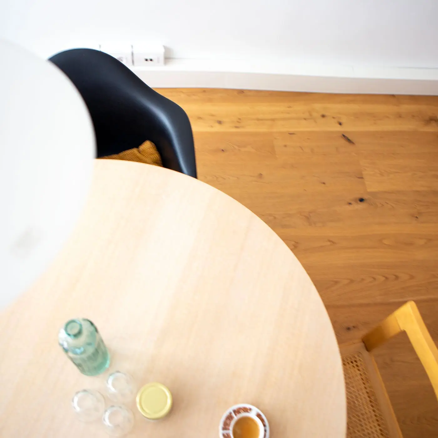 Runder heller Tisch mit grüner Glasflasche, drei Wassergläsern und einer Kaffeetasse.