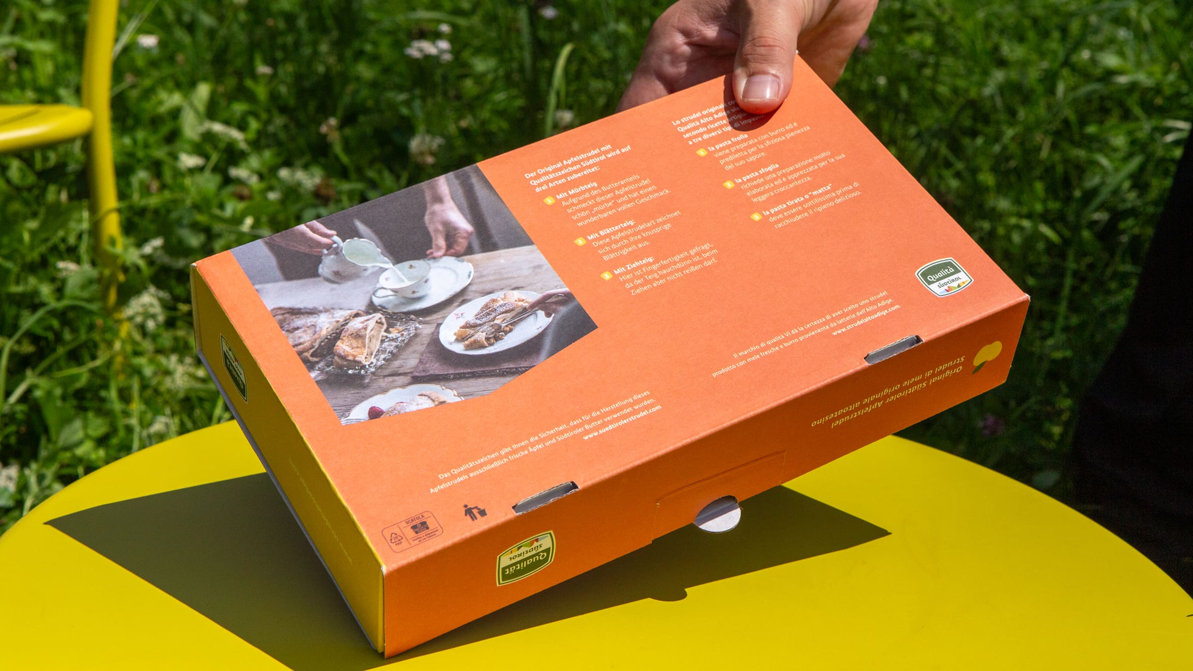 Kartonverpackung für Apfelstrudel mit Produktfoto, Rezepten und orangem Hintergrund.