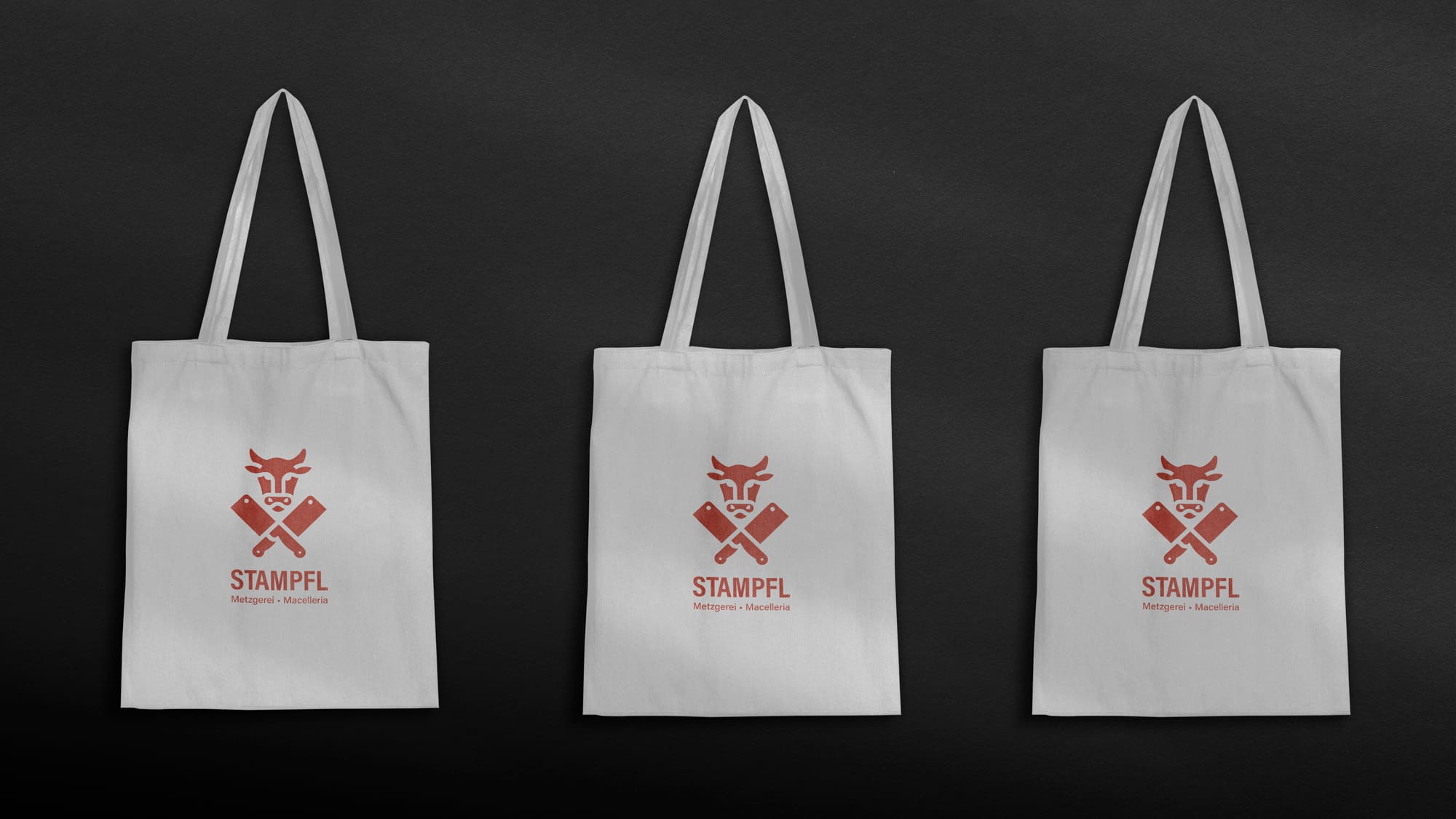 Drei weiße Stofftaschen mit aufgedrucktem Logo der Metzgerei Stampfl.