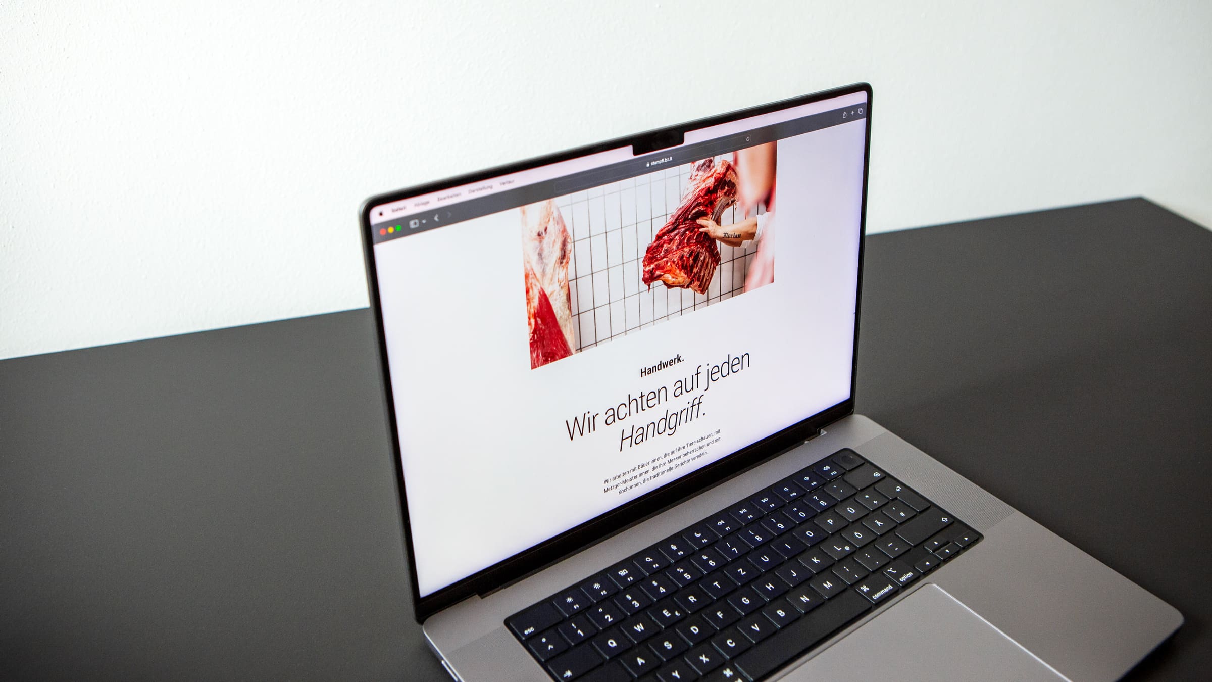 Laptop, der die Website der Metzgerei Stampfl anzeigt. Darauf ist Text und ein Foto von Fleischhälften zu sehen.